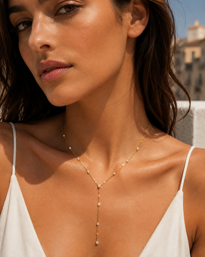 Model wears the gold Soleil Y NECKLACE with its crystal lariat drop close to the neckline, in a sunlit portrait.