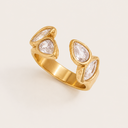 Gold open ring set with four bezel pear and marquise zirconia stones along the band, on a cream backdrop — Folie à Trois Solene RING.