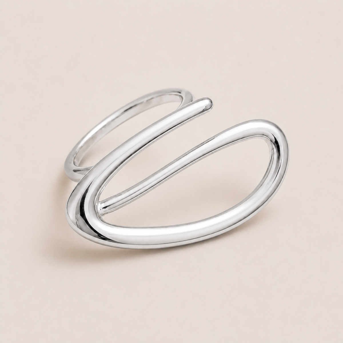 Silver open ring with a looping wire spiral forming an elongated oval, shown in close-up on a cream backdrop — Folie à Trois Solstice RING.