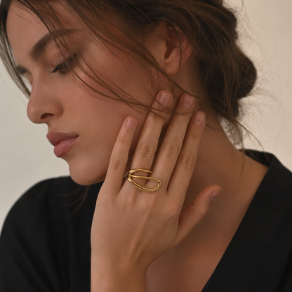 Model wears the gold Solstice RING's looping oval spiral on her finger, hand raised to her cheek.