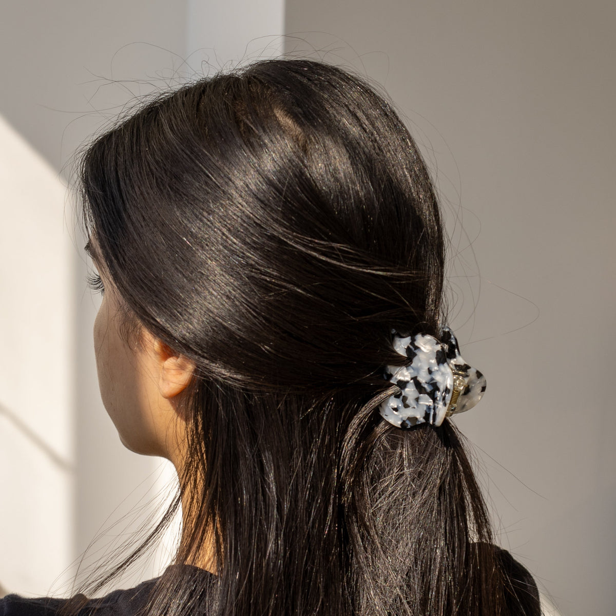 A woman wearing the black and white mottled Soul On The Line HAIR CLIP in a low ponytail, side profile in sunlight.