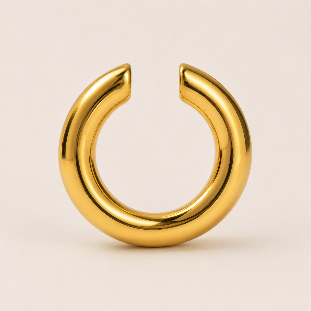 The Sperlonga EAR CUFF in gold, a smooth open-ended tube cuff shown in a studio flat lay on cream.