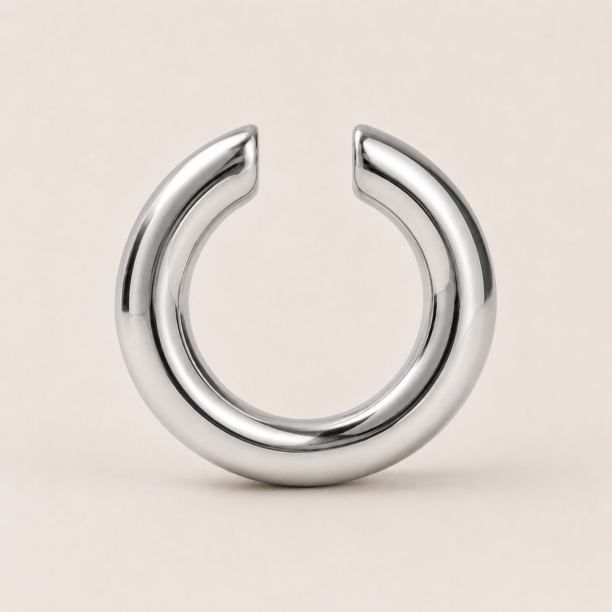 The Sperlonga EAR CUFF in silver, a smooth open-ended tube cuff shown in a studio flat lay on cream.