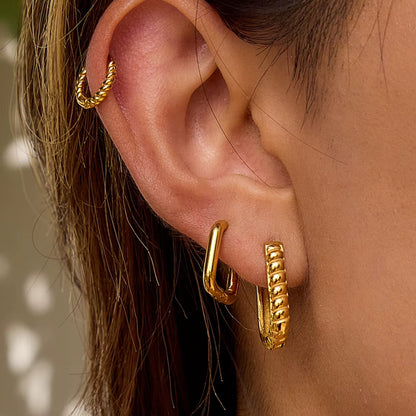 St. Moritz Earrings worn on the ear as a ridged gold hoop stacked beneath a twisted-rope cartilage cuff, adding texture to the lobe.