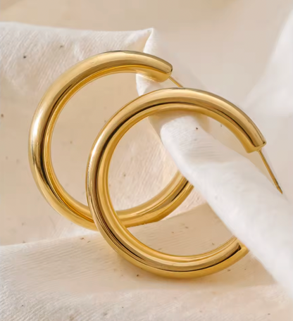 Statement Hoop earrings styled on a soft white fabric, showing the thick polished gold tube up close.