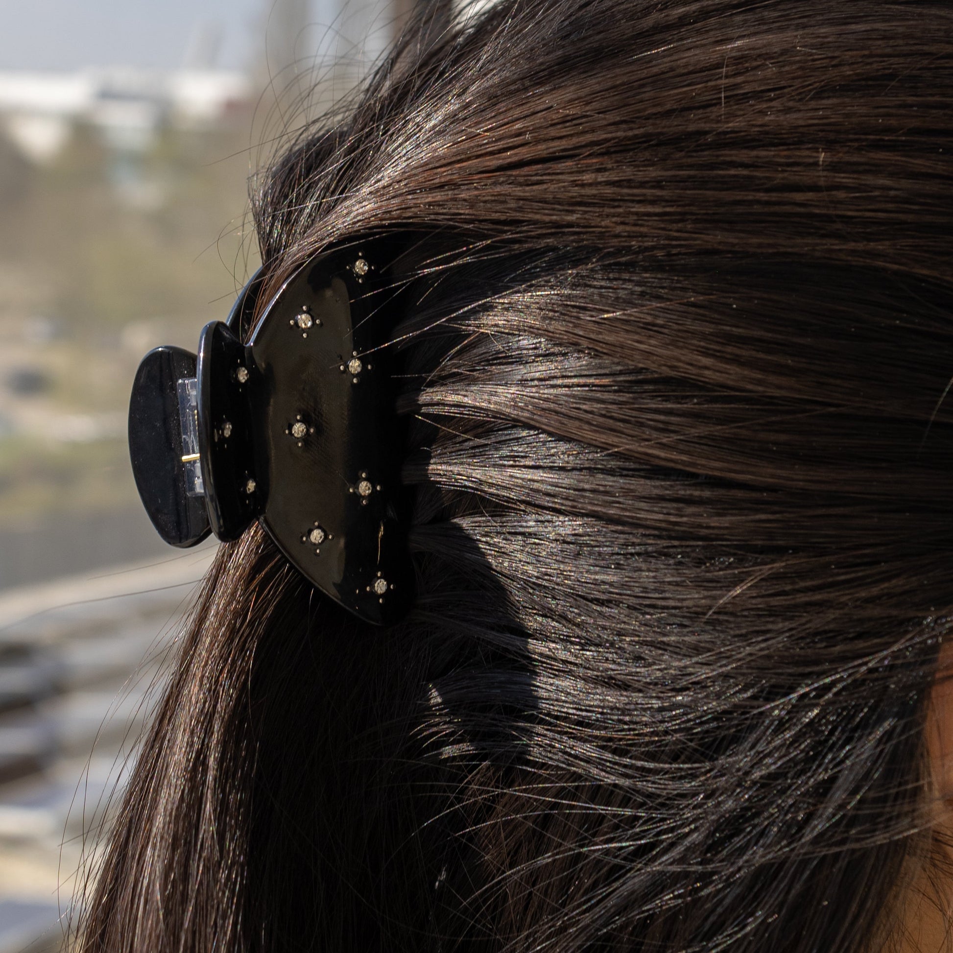 Summer Bliss HAIR CLIP in solid black, worn holding a low ponytail on dark hair, close-up side view.