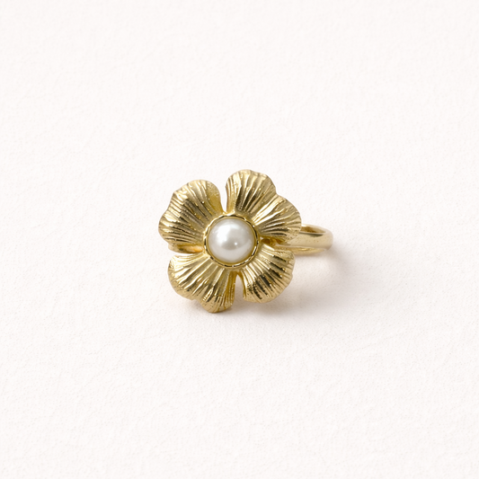 Gold ring shaped like a textured five-petal flower with a pearl center, shown at an angle on a cream backdrop — Summertime Harmony RING.