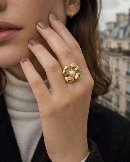 Close-up of a hand near the face wearing the gold textured flower Summertime Harmony RING with its pearl center, city backdrop.