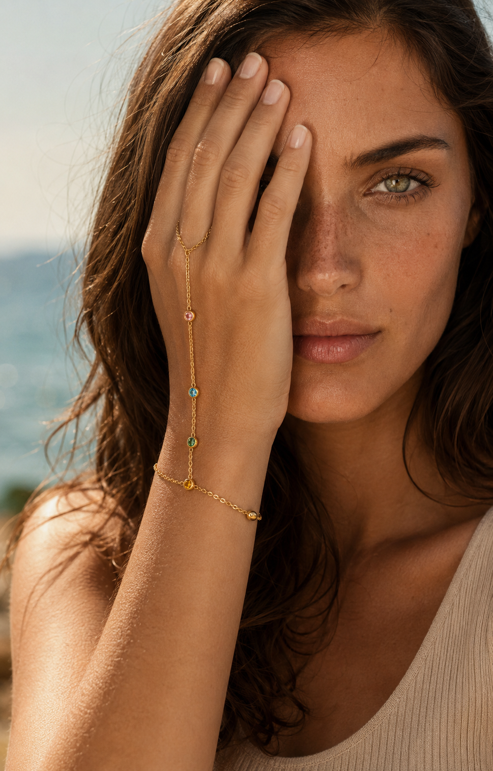 Sunlit Hand Chain BRACELET worn on the hand with colorful gemstones catching light, model covering one eye at the beach.