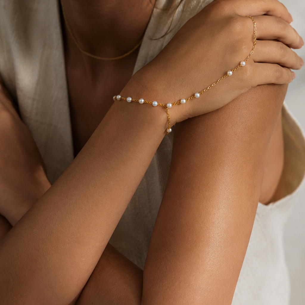 Sunseeker Hand Chain BRACELET worn on the hand with arms crossed, pearls catching light against tan skin.