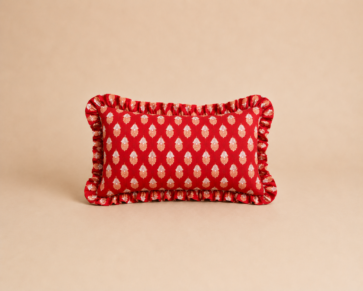 Sunset Motif Rectangle cushion in red with a repeating cream and orange paisley leaf print and a ruffled border on a warm backdrop.