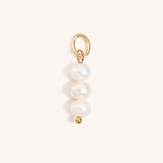 The Sweet Water Pearls CHARM in a flat lay, three stacked freshwater pearls on a gold paperclip connector on cream fabric.