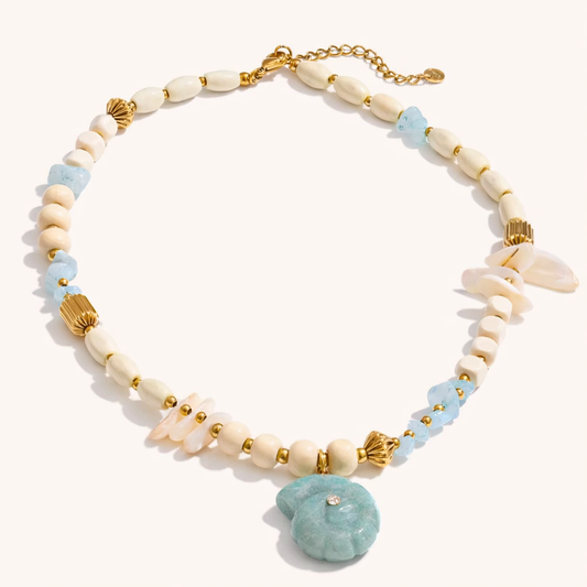 The Tahiti NECKLACE laid flat, showing cream wood and shell beads, aquamarine chips, and gold accents around a carved shell pendant.