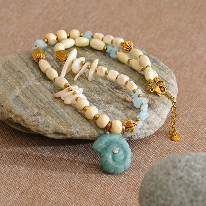 The Tahiti NECKLACE coiled on a stone surface, its gold lobster clasp and extender chain visible alongside the beaded strand.