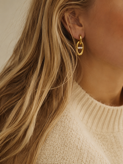 Model wears the gold Folie à Trois Talia EARRINGS, an oval chain-link drop earring, styled with a cream knit sweater.