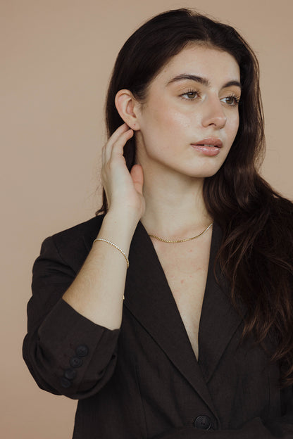 The Tennis NECKLACE worn as a choker at the neckline, the sparkling stone chain layered under a dark blazer collar.