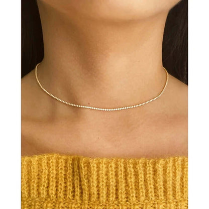 The Tennis NECKLACE in gold worn as a choker at the neckline, sparkling stones set close along the throat.