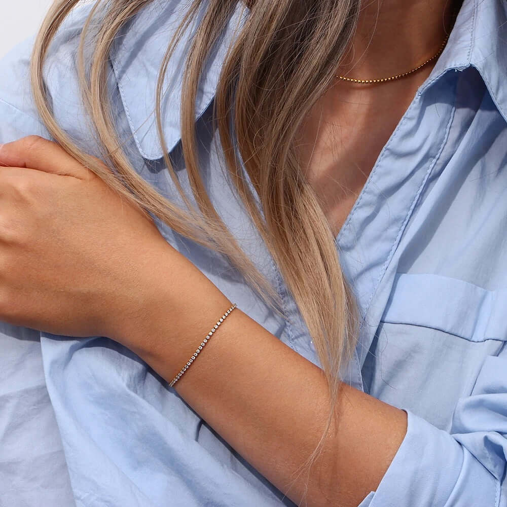 The Tennis NECKLACE in gold worn faintly at the neckline, paired with a matching tennis bracelet on the wrist.