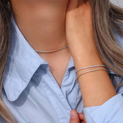 The Tennis NECKLACE in silver worn as a choker, layered above a matching tennis bracelet stacked on the wrist.
