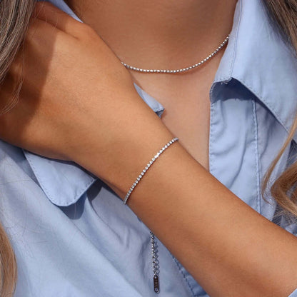 The Tennis NECKLACE in silver worn close at the neckline, paired with a matching tennis bracelet on the raised wrist.