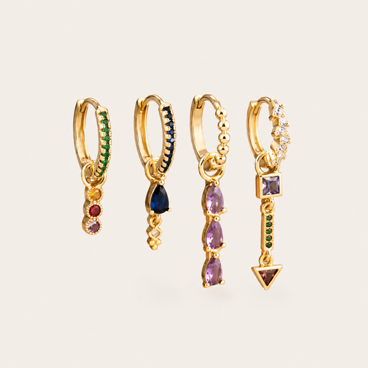 Tessa Set of four gold huggie hoops with dangling charms in emerald, sapphire, amethyst, and mixed gemstone drops.