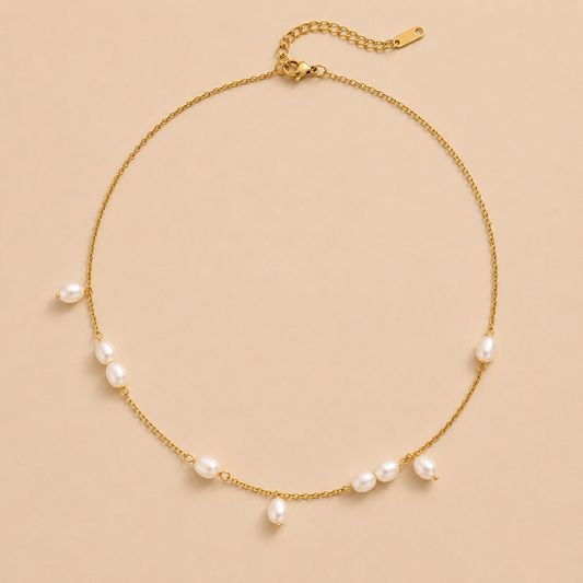 Gold chain necklace with scattered freshwater pearl drops from the Thalassa NECKLACE design, laid flat on a beige background.