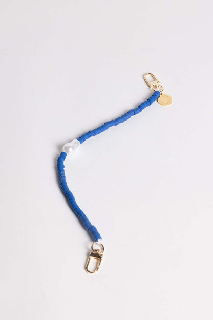 A blue heishi bead phone cord with a white pearl-style bead and gold clasps, shown on a white background.