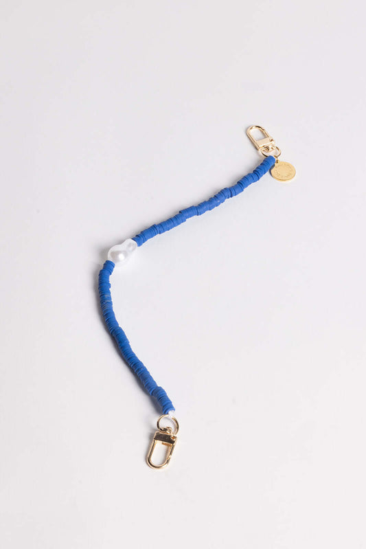 A blue heishi bead phone cord with a white pearl-style bead and gold clasps, shown on a white background.