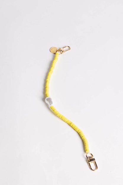 A yellow heishi bead phone cord with a white bead and gold clasps, shown on a white background.
