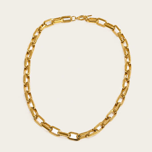 Gold chunky chain necklace with rectangular links from the Resort Edit NECKLACE design, laid flat on a beige background.