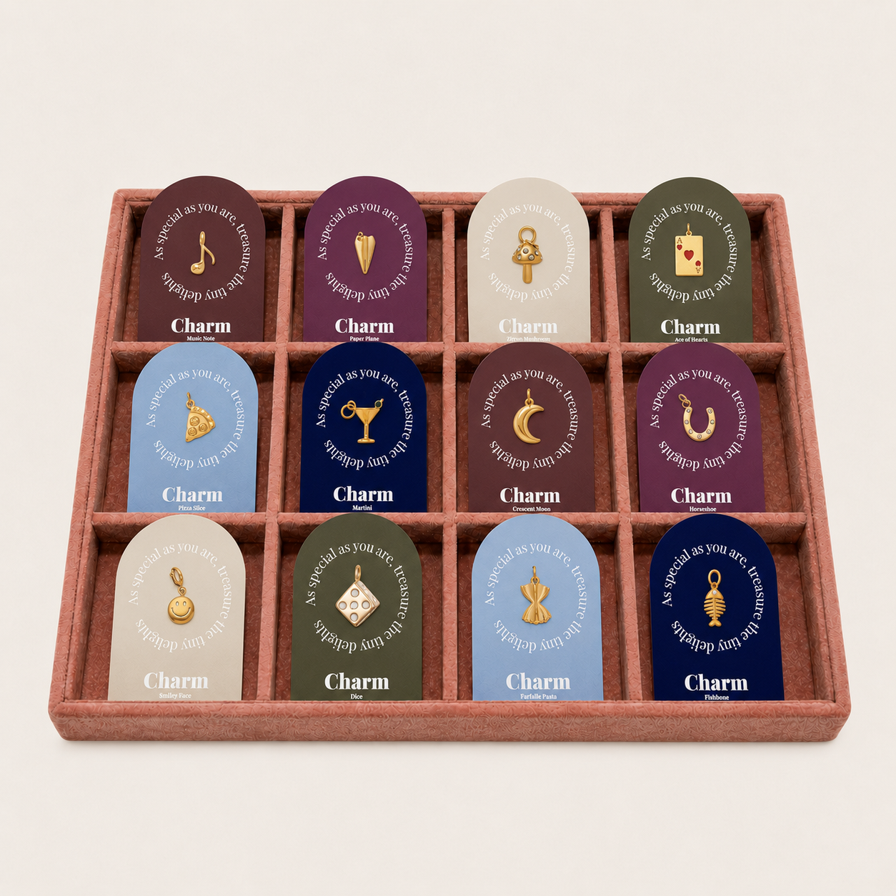 The Signature Charms BUNDLE displayed as twelve gold charm cards arranged in a terracotta velvet tray on a beige background.