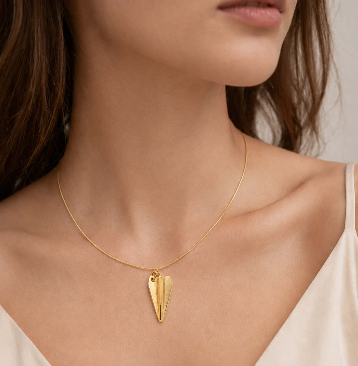 Gold paper airplane charm from the Signature Charms BUNDLE worn on a fine gold chain, shown close to the neckline.