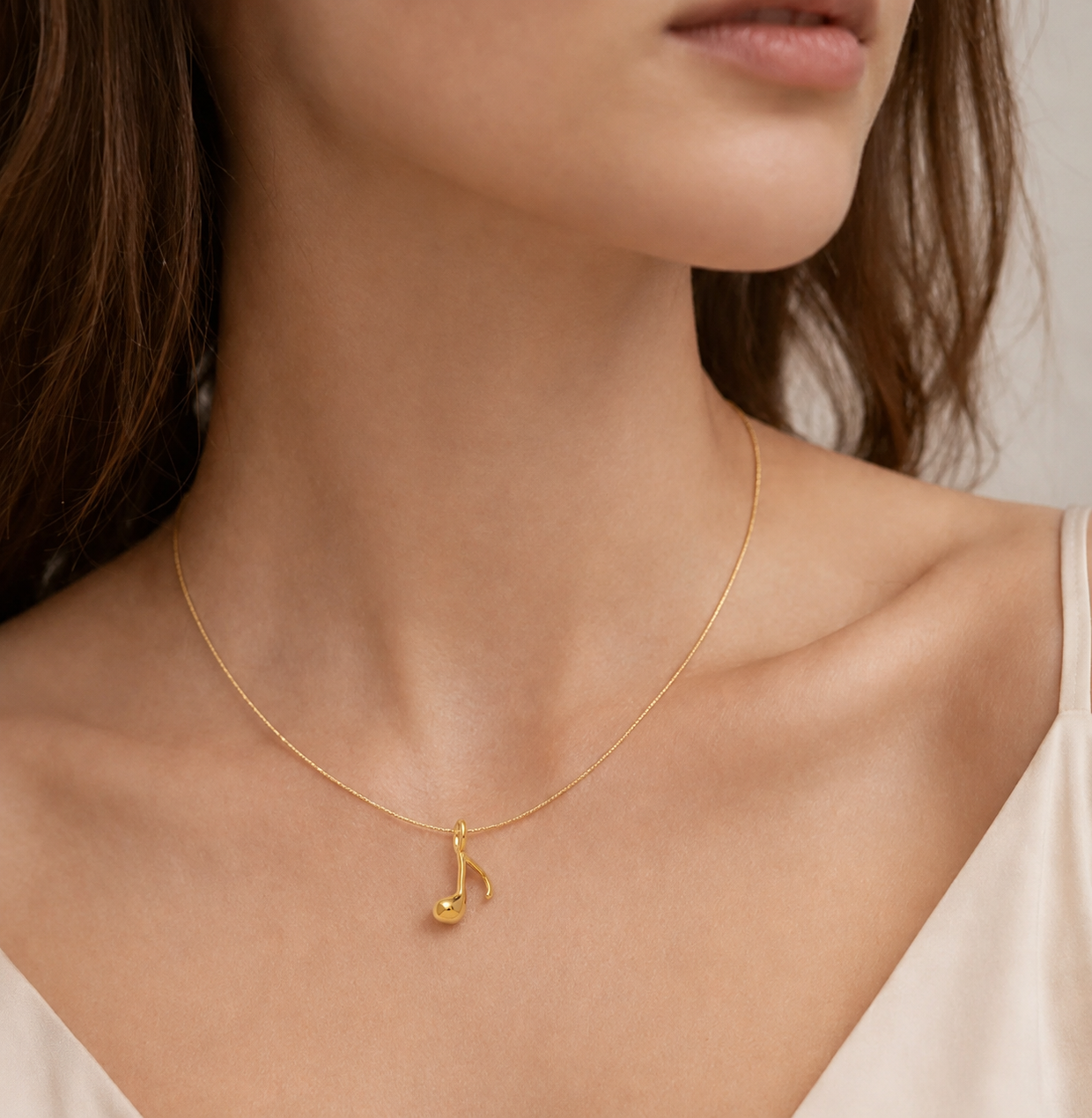 Gold music note charm from the Signature Charms BUNDLE worn on a fine gold chain, shown close to the neckline.