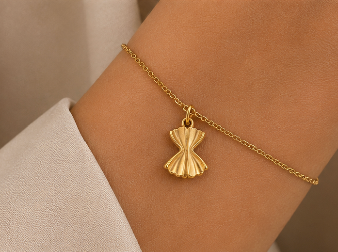 Gold farfalle pasta charm from the Signature Charms BUNDLE worn on a chain bracelet, close-up on the wrist.