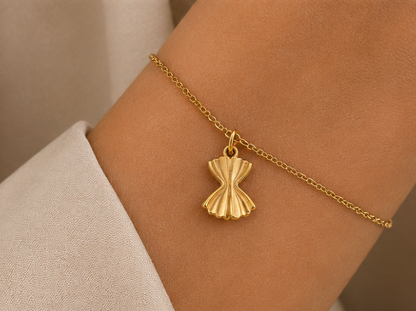 Gold farfalle pasta charm from the Signature Charms BUNDLE worn on a chain bracelet, close-up on the wrist.