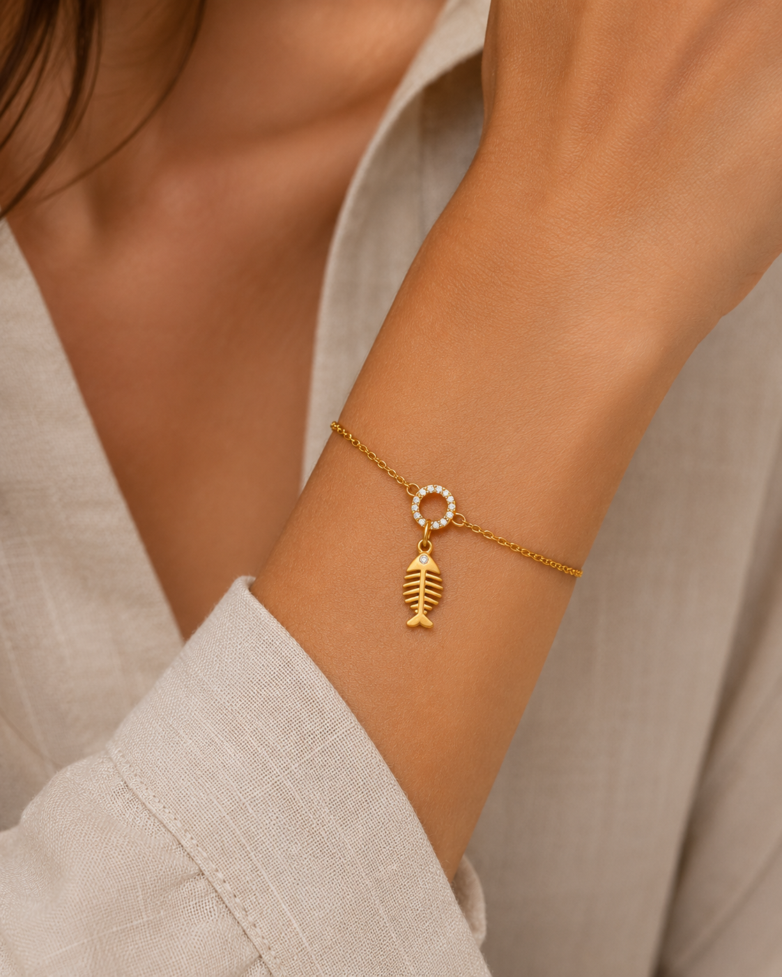 Gold fishbone charm with a pave circle link from the Signature Charms BUNDLE, worn on a chain bracelet on the wrist.
