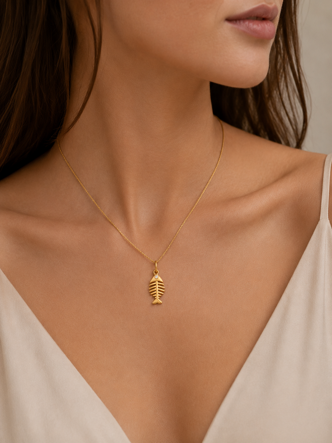 Gold fishbone charm from the Signature Charms BUNDLE, worn on a fine gold chain necklace close to the neckline.