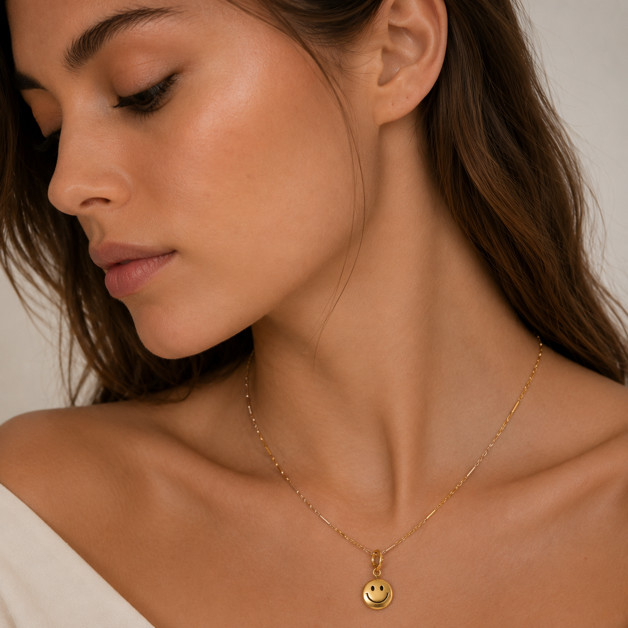 Gold smiley face charm from the Signature Charms BUNDLE, worn on a gold figaro-style chain close to the neckline.
