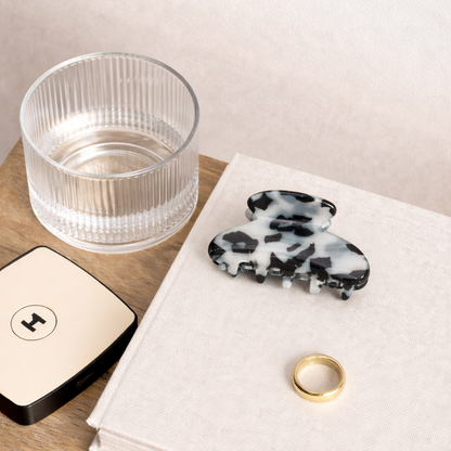 The Till Sun Up HAIR CLIP styled flat lay on a book beside a ribbed glass, a gold ring and a compact mirror.
