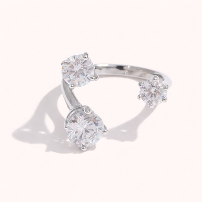 Open silver ring set with three round clear stones at different heights, shown at an angle on a cream backdrop.