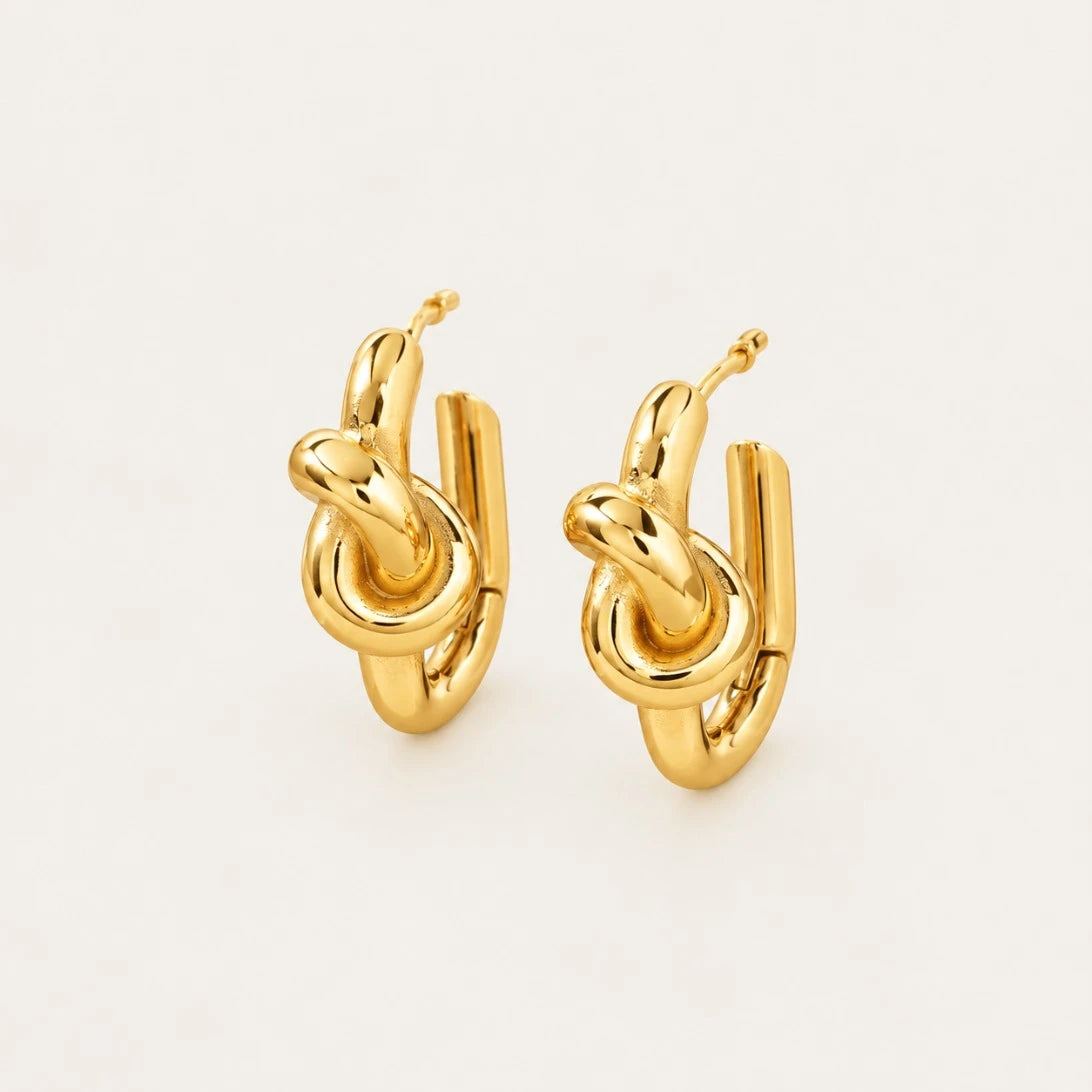 Front view of gold Twine EARRINGS with a polished knotted design on a cream background — Folie à Trois wholesale jewelry