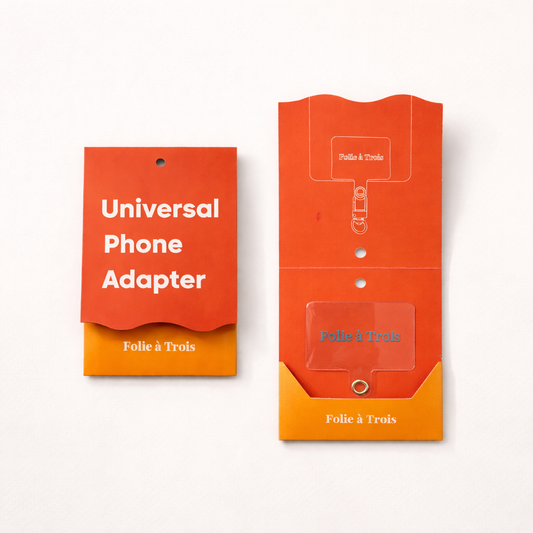 Universal Phone Adapter packaging tag and matching envelope sleeve, both printed with the Folie à Trois logo, laid flat side by side.
