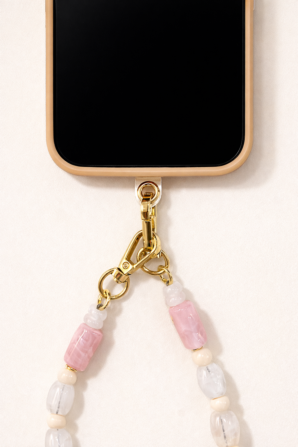 Close-up of the Universal Phone Adapter gold clasp attaching a white, pink, and coral beaded strap to a cream phone case.