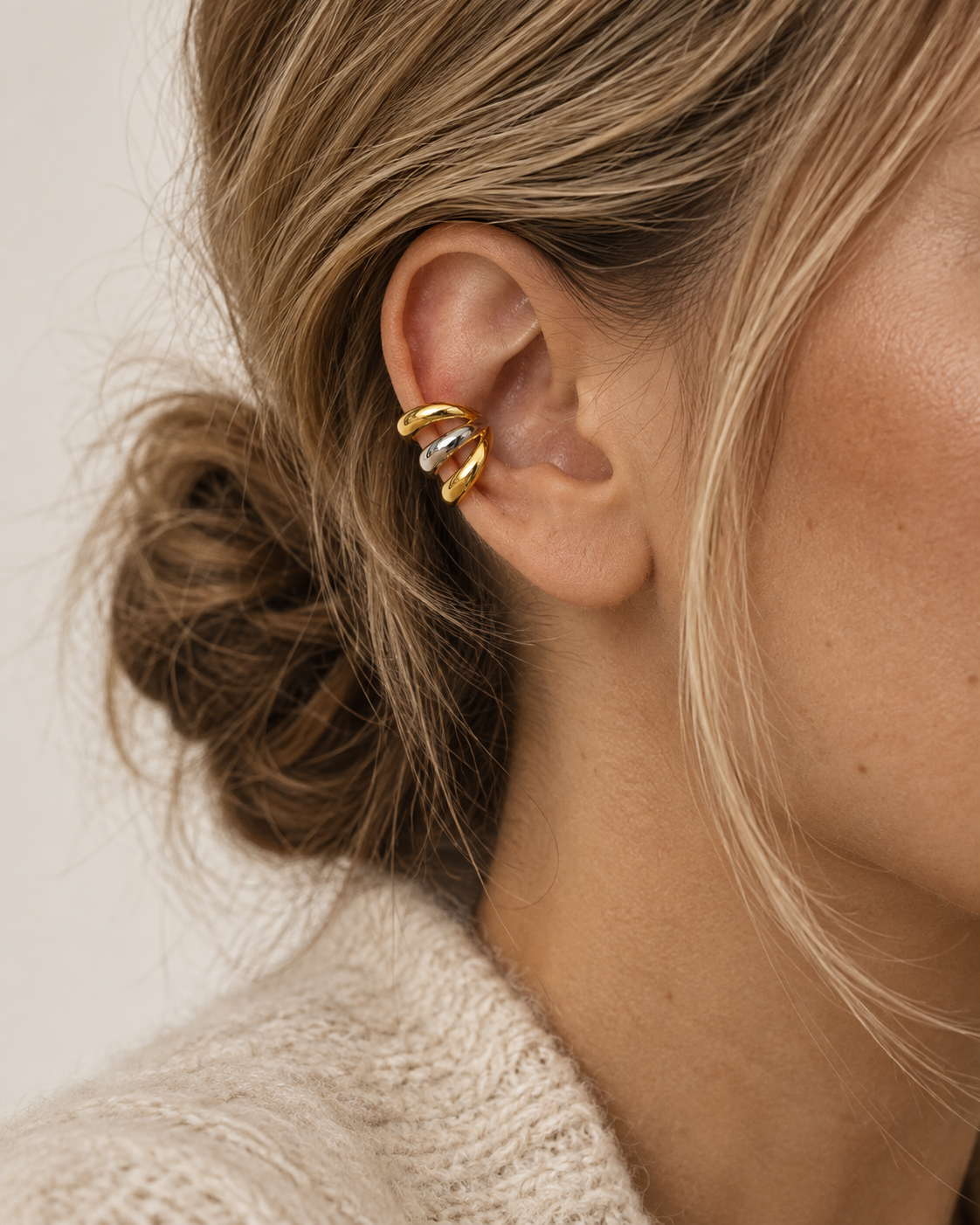 Gold and silver two-tone triple-band ear cuff worn on a model's ear against a cream sweater — Folie à Trois Unruly EAR CUFF.