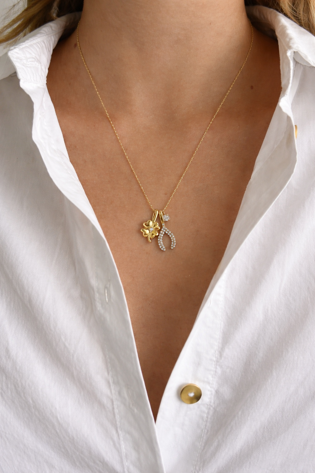 The Untamed NECKLACE worn at the neckline over a white shirt, its clover and pave wishbone charms resting together.
