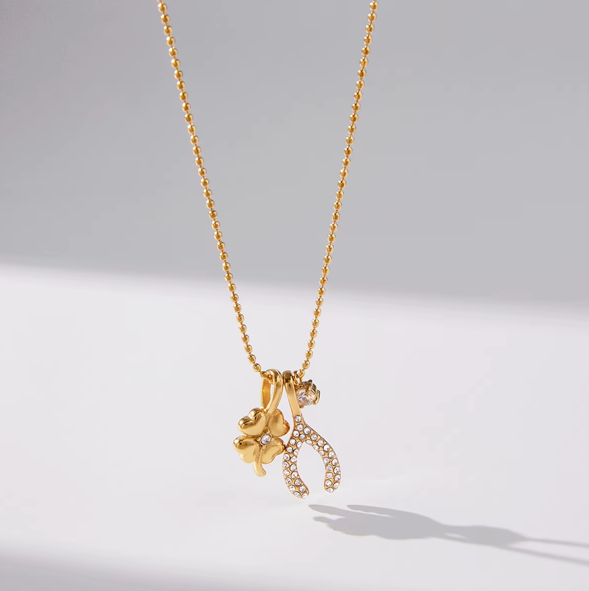 The Untamed NECKLACE hanging close-up, its gold clover and crystal-set wishbone charms catching soft studio light.