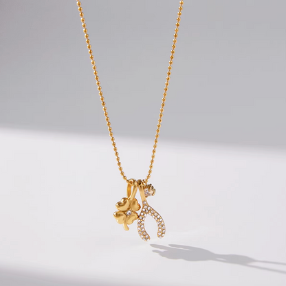 The Untamed NECKLACE hanging close-up, its gold clover and crystal-set wishbone charms catching soft studio light.