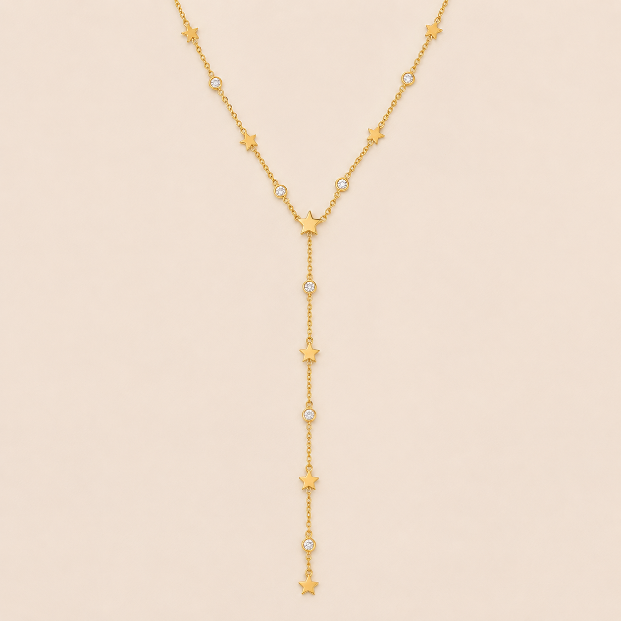 Gold Vagabonde Y NECKLACE with star and crystal stations drawn into a long lariat drop, laid flat on a beige background.