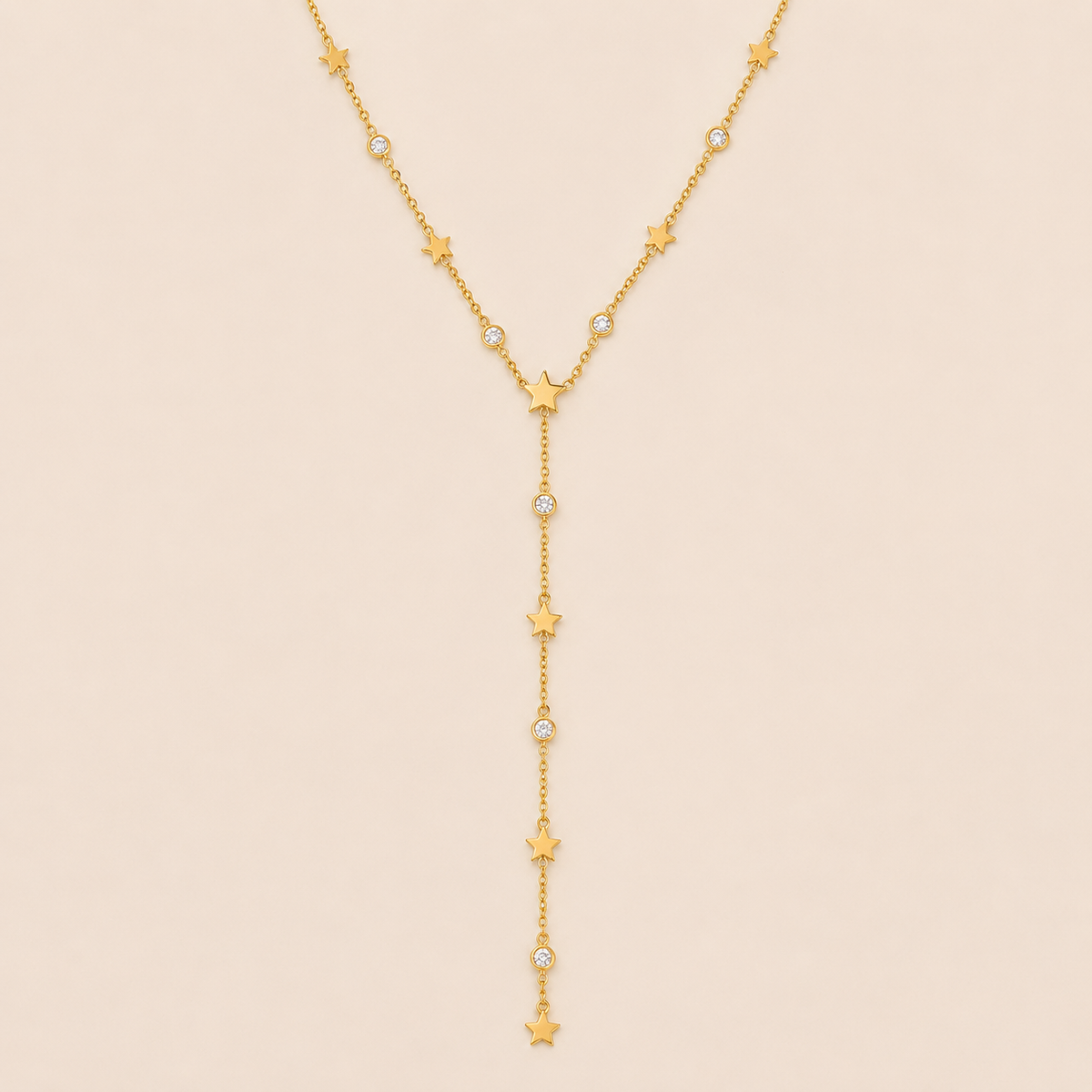 Gold Vagabonde Y NECKLACE with star and crystal stations drawn into a long lariat drop, laid flat on a beige background.