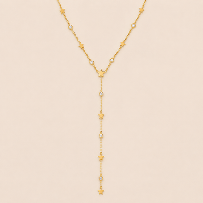 Gold Vagabonde Y NECKLACE with star and crystal stations drawn into a long lariat drop, laid flat on a beige background.